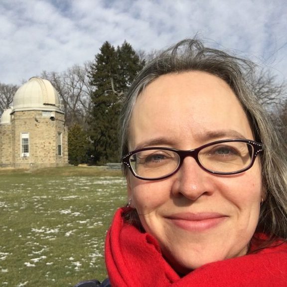A women
							with glasses
							and a red
							scarf in front
							of an old
							stone observatory